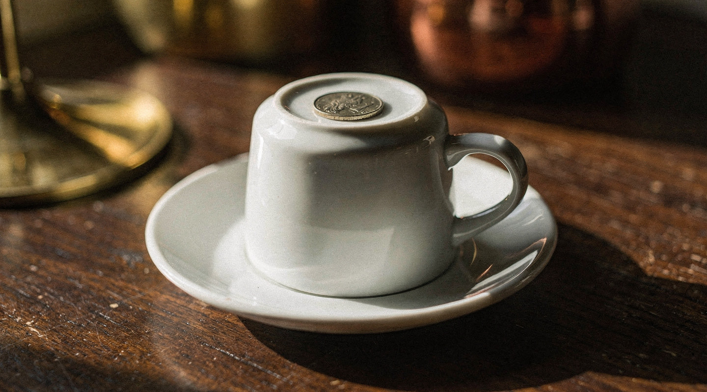 An upturned coffee cup resting on its saucer with a small coin placed on the base