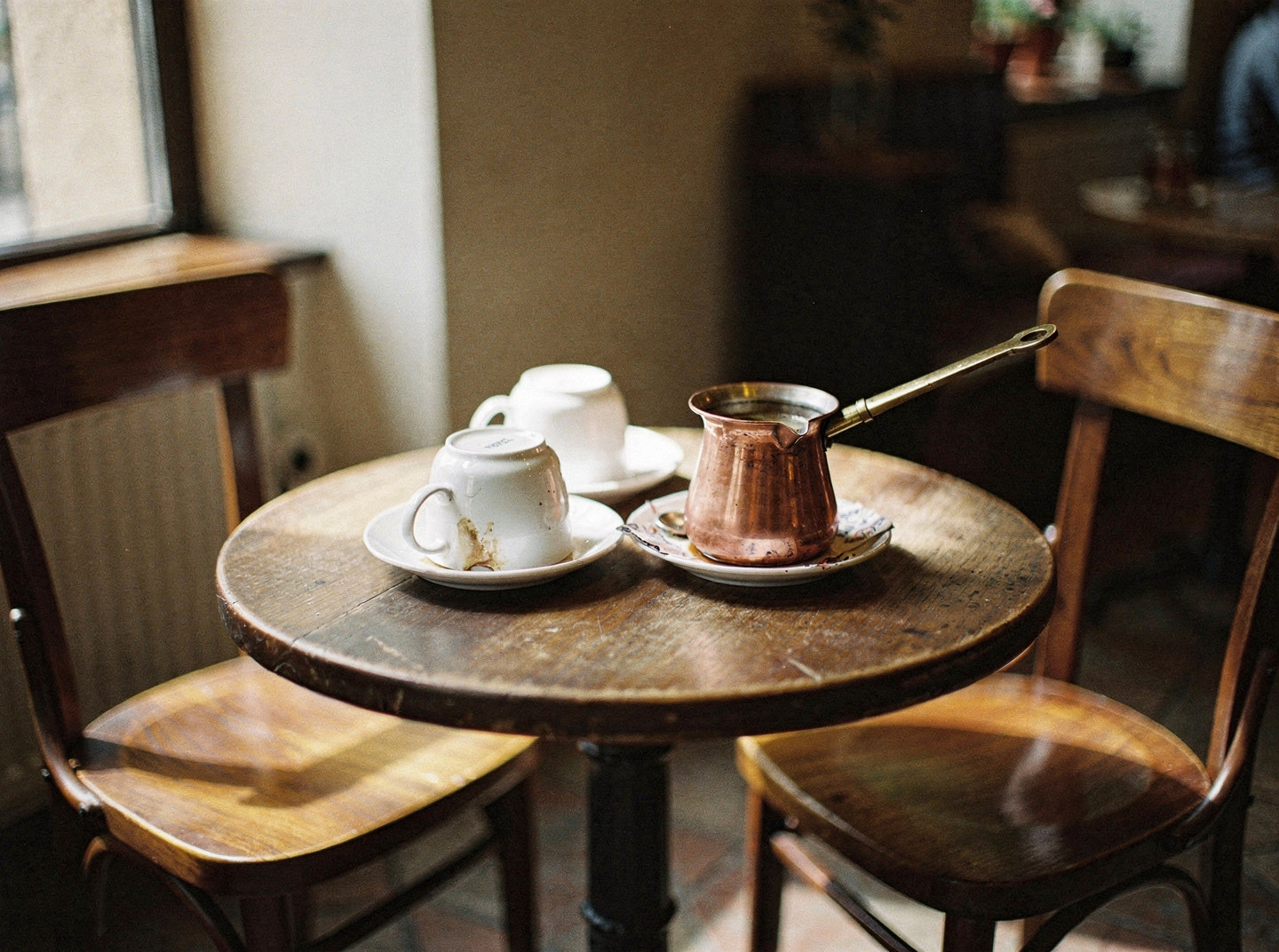 Two chairs pulled up to a small table holding two upturned cups and a copper cezve