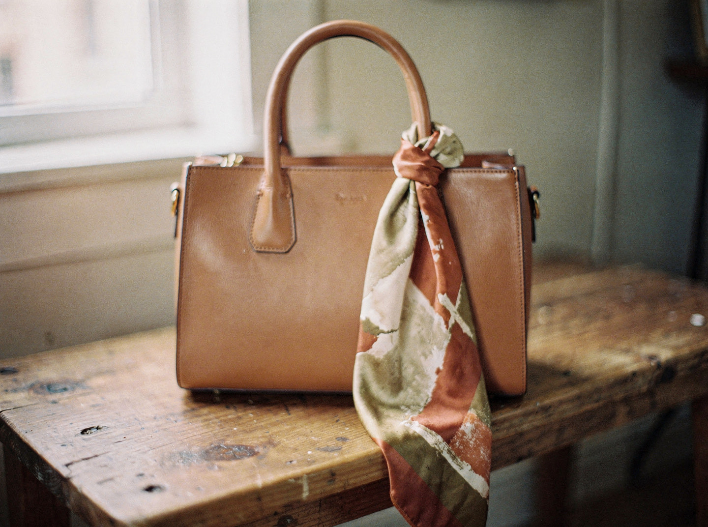 A silk scarf knotted around the leather handle of a structured handbag
