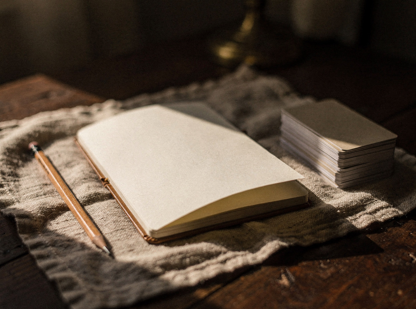 An open notebook, a pencil, and a small stack of cards on a linen cloth in warm afternoon light