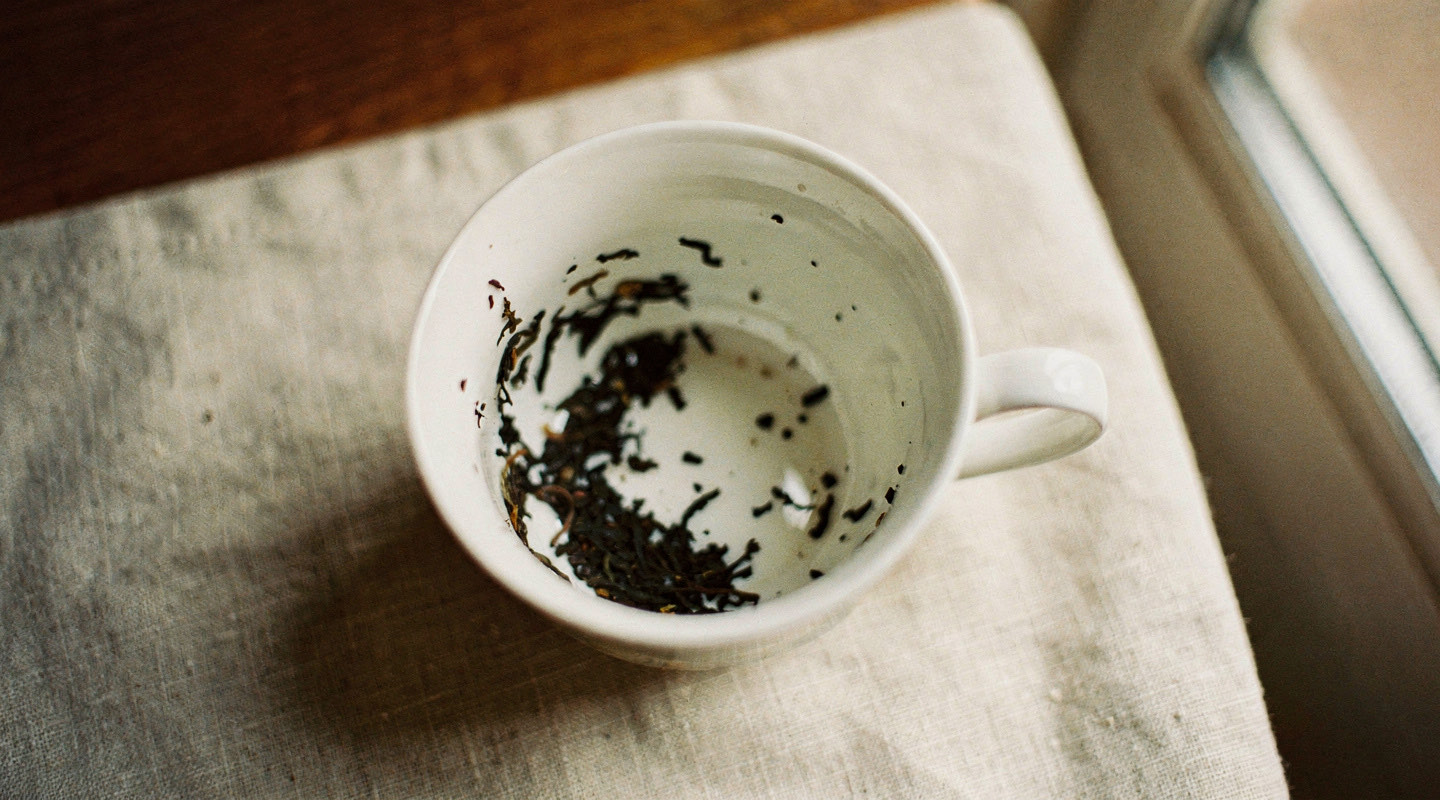 The inside of a white teacup showing scattered dark tea leaves against the porcelain
