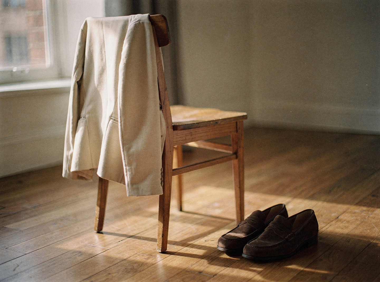 A light jacket over a chair beside a pair of brown suede loafers in warm morning light