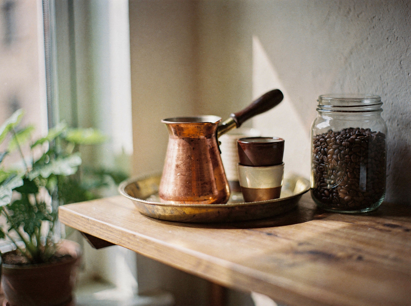 A small tray of coffee things on a kitchen shelf beside a window in soft morning light