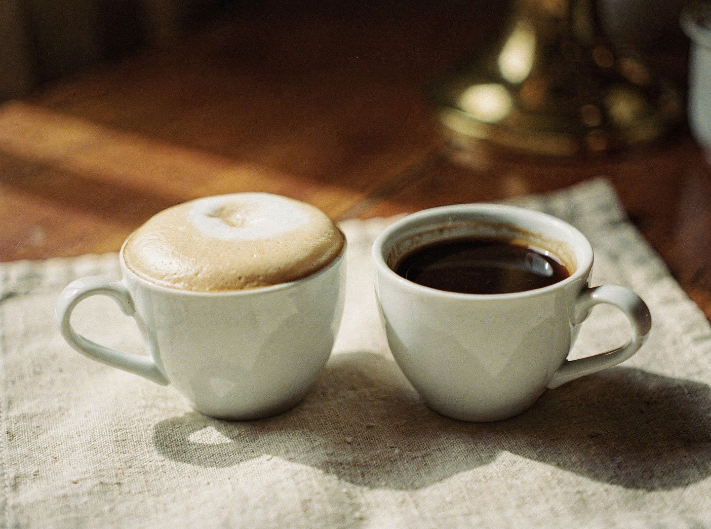Two small porcelain cups side by side, one topped with thick foam and one flat and dark